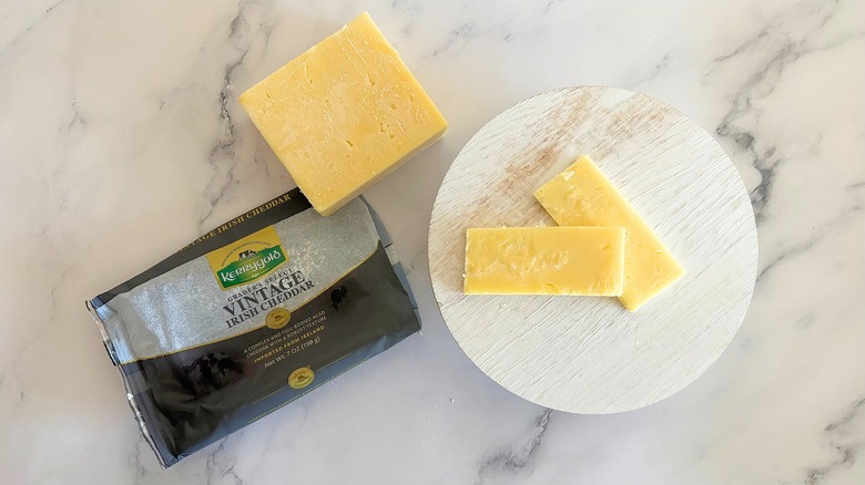 Block of Kerrygold Vintage Irish Cheddar next to packaging and cheese slices on marble surface