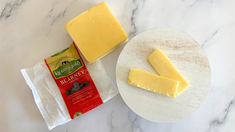 Block of Kerrygold Blarney Cheese next to packaging and cheese slices on marble surface