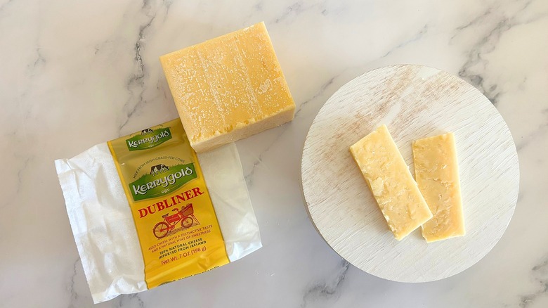 Block of Kerrygold Dubliner Cheese next to packaging and cheese slices on marble surface