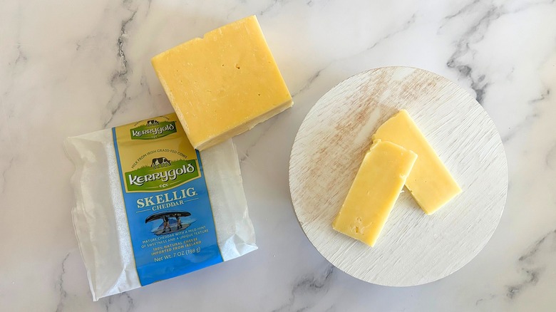 Block of Kerrygold Skellig Cheddar next to packaging and cheese slices on marble surface