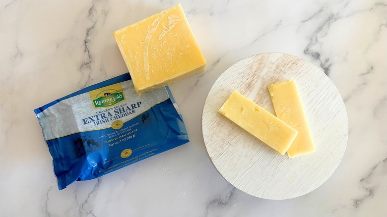 Block of Kerrygold Extra Sharp Irish Cheddar next to packaging and cheese slices on marble surface