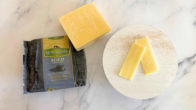 Block of Kerrygold Aged Cheddar next to packaging and cheese slices on marble surface