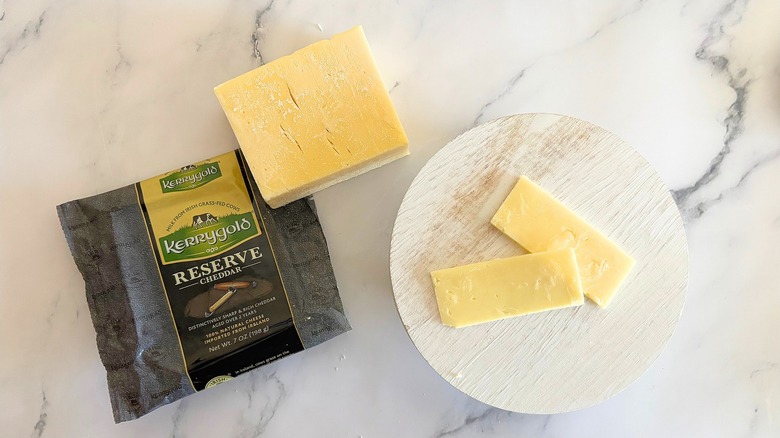 Block of Kerrygold Reserve Cheddar next to packaging and cheese slices on marble surface