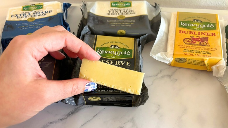 Hand holding slice of Kerrygold cheese above packages of cheese on marble surface
