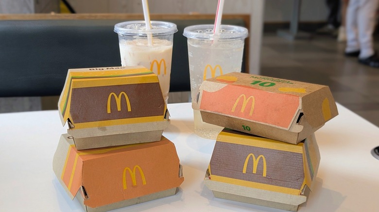 Cardboard boxes of food with the McDonald's logo on them and two drinks in plastic cups on a white table