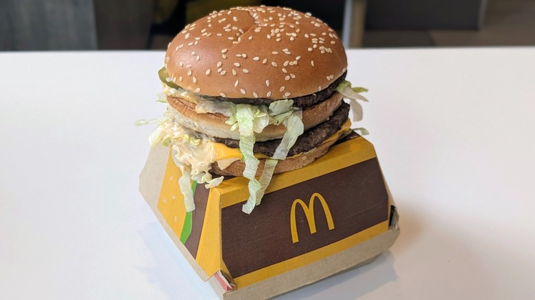 A Big Mac made with Quarter Pounder patties on top of its box on a table at McDonald's