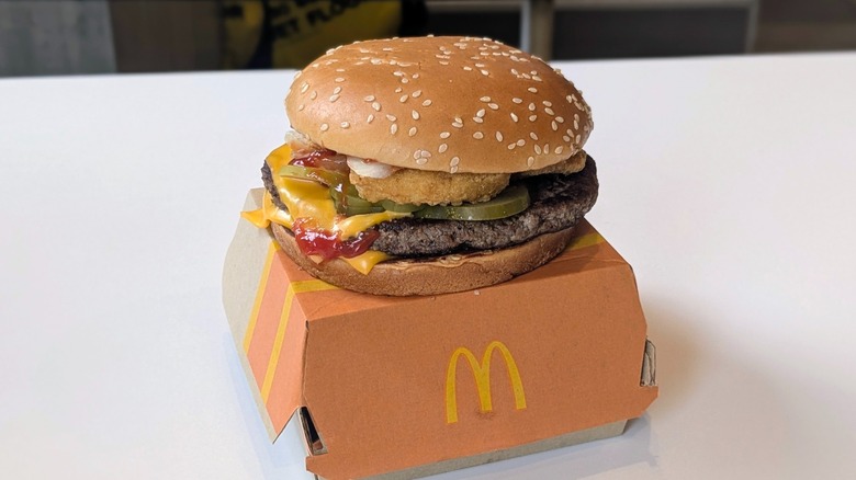 A Quarter Pounder with chicken nuggets on it on top of the box it came in on a table at McDonald's