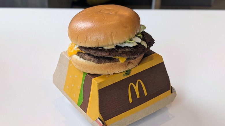 A Big Mac with a steamed bun on top of its box on a table at McDonald's