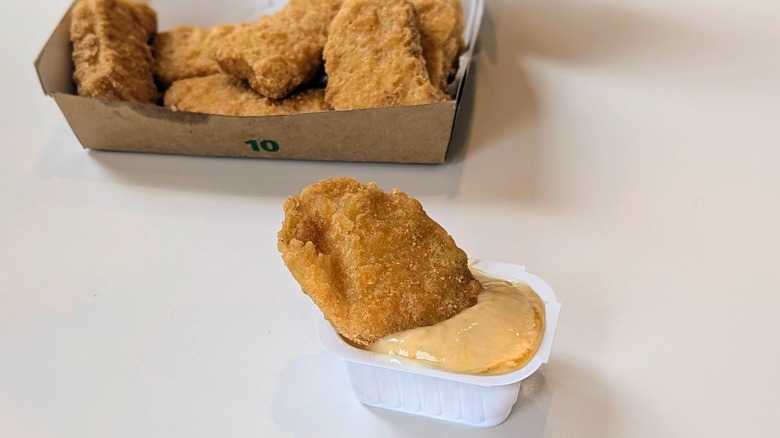 A plastic cup of sweet and sour sauce mixed with mayo with a McNugget sticking out of it and a box of nuggets in the background