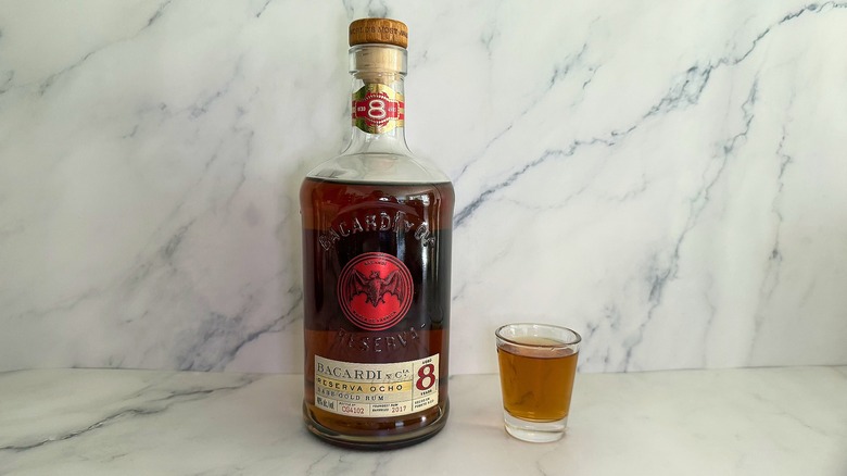 Bottle of Bacardí Reserva Ocho next to shot glass on marble surface