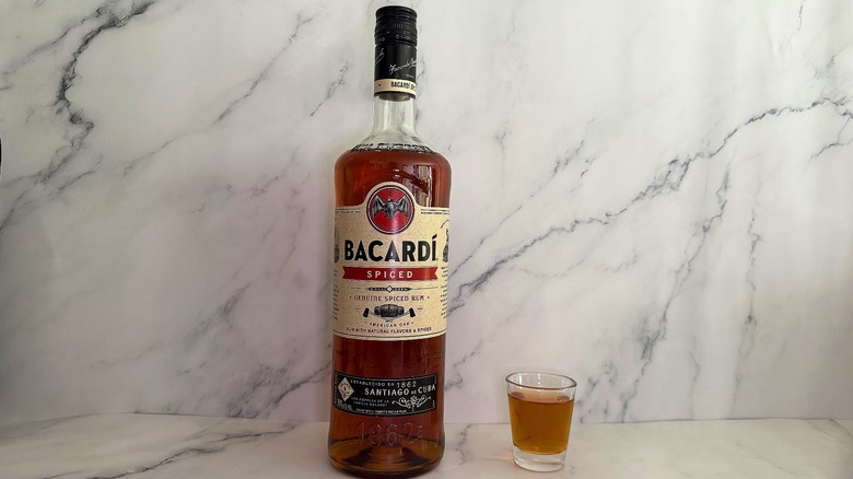 Bottle of Bacardí Spiced next to shot glass on marble surface