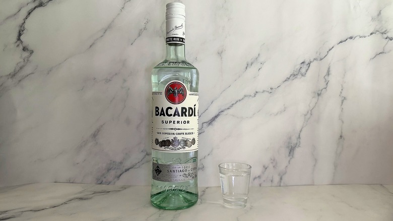 Bottle of Bacardi Superior next to shot glass on marble surface