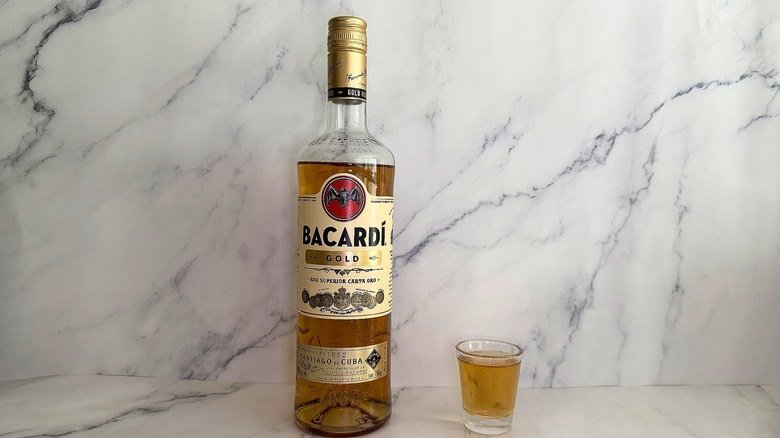 Bottle of Bacardí Gold next to shot glass on marble surface
