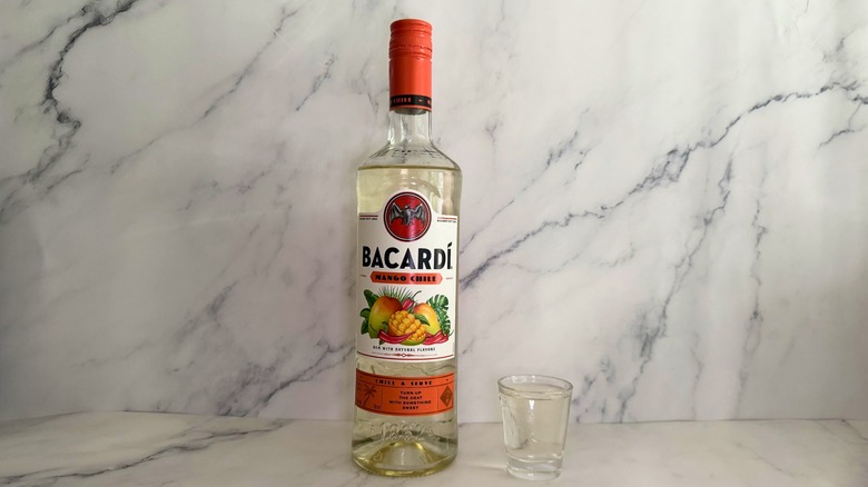 Bottle of Bacardí Mango Chile next to shot glass on marble surface