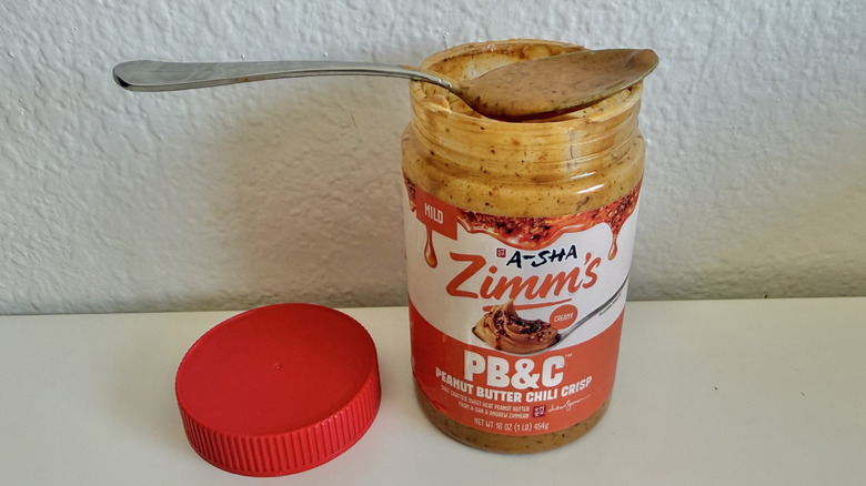 A-Sha Foods Zimm's Chili Crisp peanut butter jar with spoon on top with some peanut butter inside