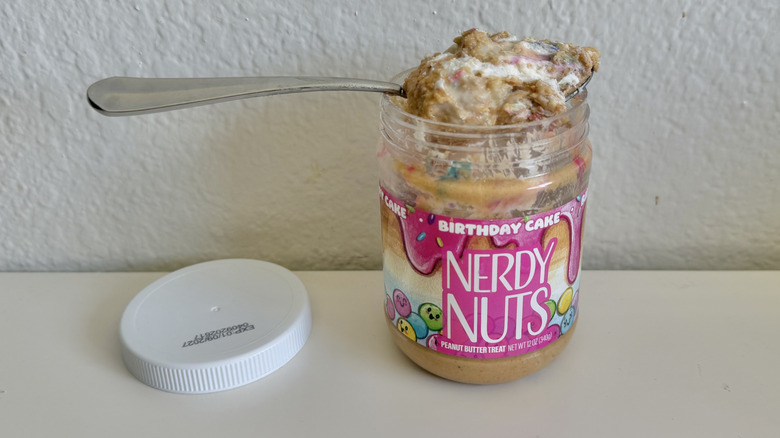 Jar of Nerdy Nuts Birthday Cake Peanut Butter Treat with spoon on a white table