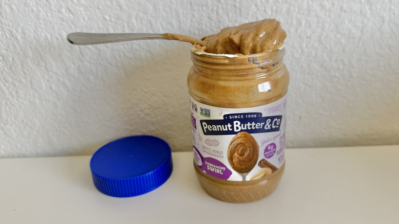 Jar of Peanut Butter & Co. Cinnamon Swirl peanut butter on a table and a spoon on top