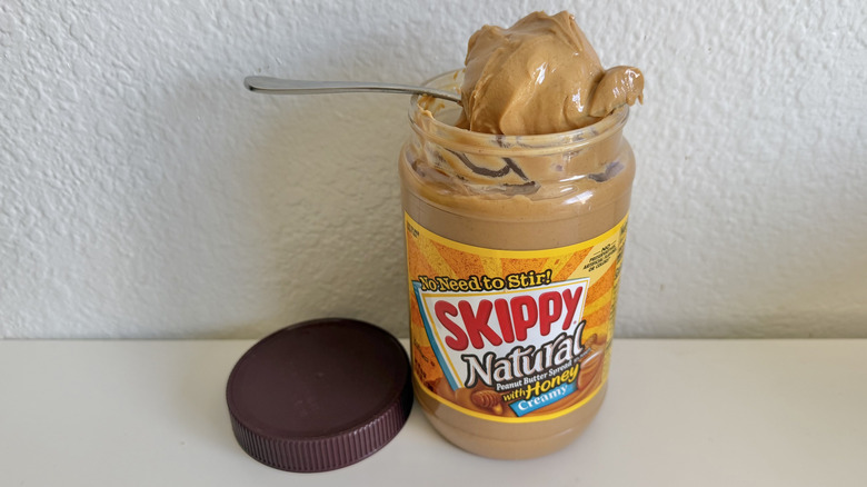 Skippy honey peanut butter jar on a table with a spoonful on top