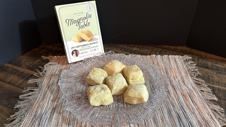 Magnolia Table buttermilk biscuits on platter and placemat on wooden table and black background.