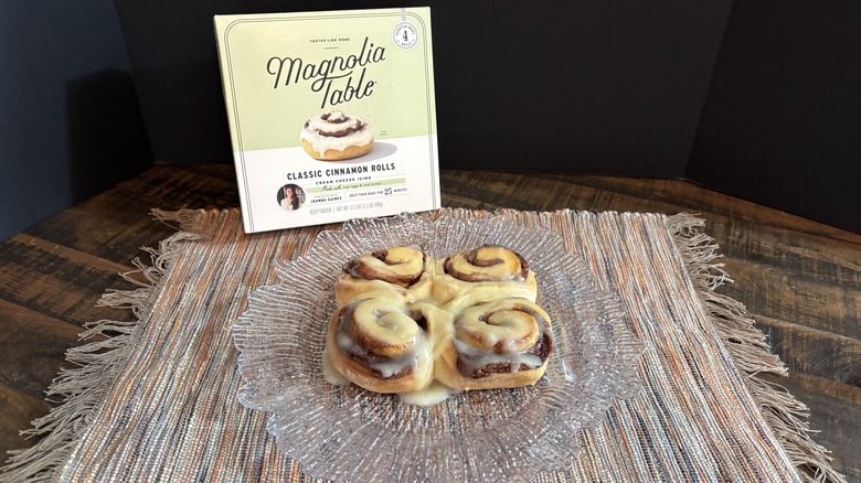 Magnolia Table cinnamon rolls on platter and placemat on wooden table and black background.
