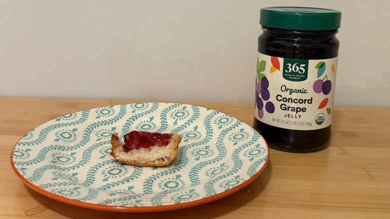 Jar of Whole Foods 354 Grape Jelly with a piece of bread and the jelly on top next to it