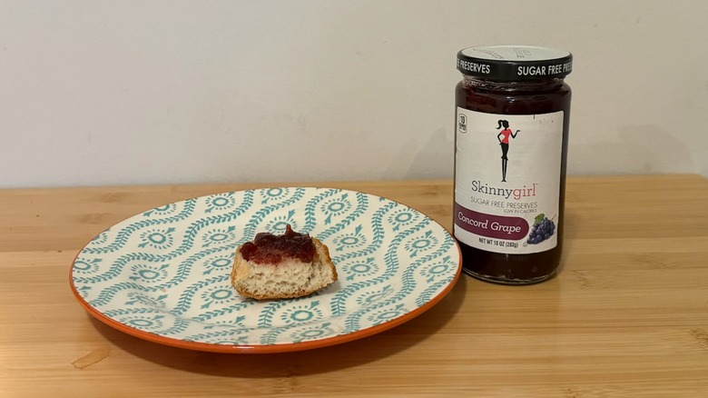 Jar of Skinny Girl Sugar Free Preserves with a piece of bread and the jelly on top next to it