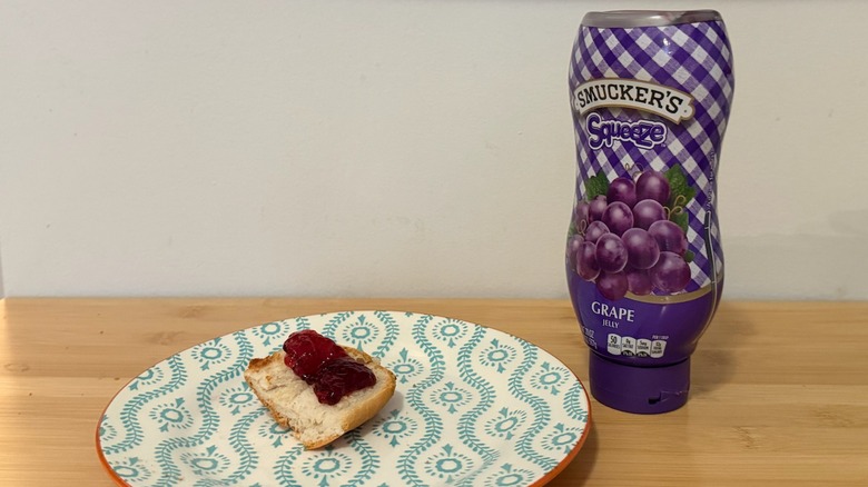 Bottle of Smucker's Grape Jelly with a piece of bread and the jelly on top next to it