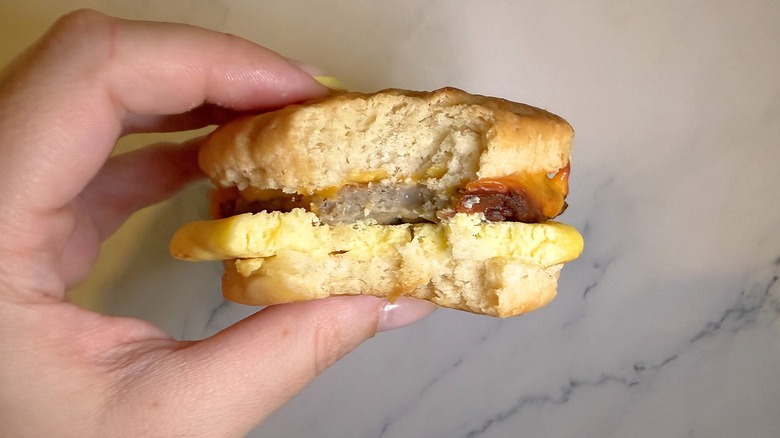 Hand holding Walmart biscuit sandwich against marble background