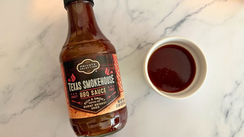 Bottle of Private Selection Texas Smokehouse BBQ Sauce on table next to small white bowl of sauce