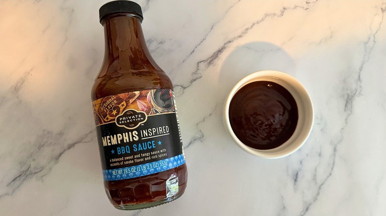 Bottle of Private Selection Memphis BBQ Sauce on table next to small white bowl of sauce