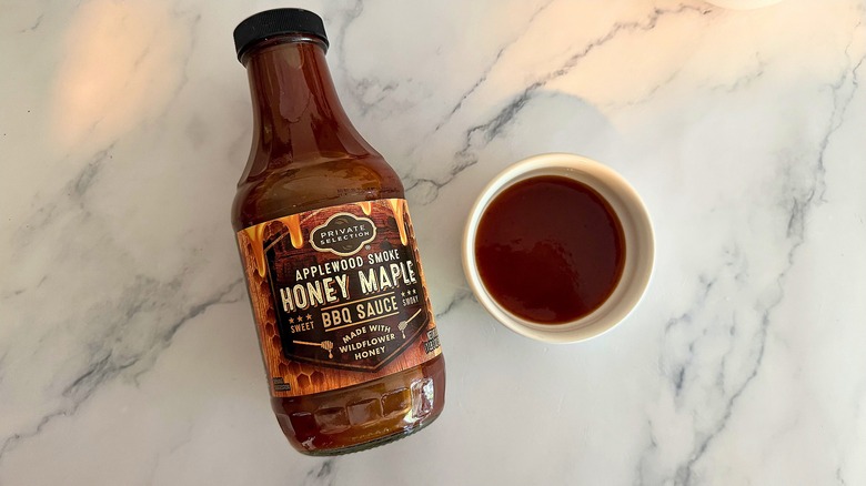 Bottle of Private Selection Applewood Smoke Honey Maple BBQ Sauce on table next to small white bowl of sauce