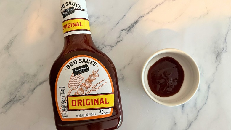 Bottle of Signature Select Original BBQ Sauce on table next to small white bowl of sauce