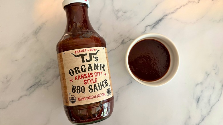 Bottle of Trader Joe's Kansas City BBQ Sauce on table next to small white bowl of sauce