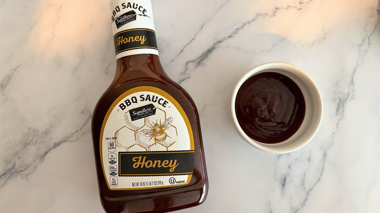 Bottle of Signature Select Honey BBQ Sauce on table next to small white bowl of sauce