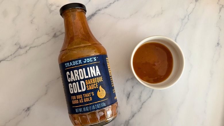 Bottle of Trader Joe's Carolina Gold BBQ Sauce on table next to small white bowl of sauce