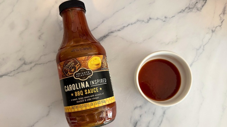 Bottle of Private Selection Carolina BBQ Sauce on table next to small white bowl of sauce