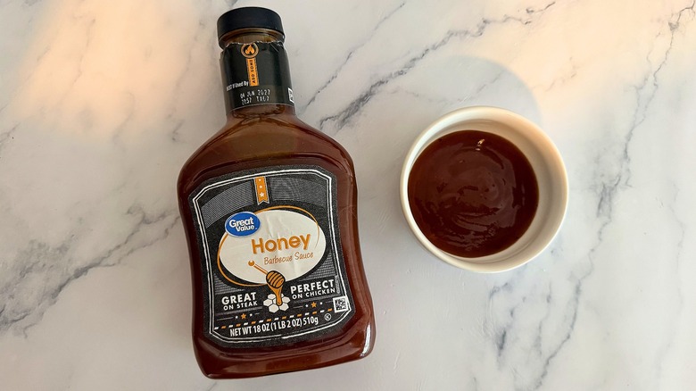 Bottle of Great Value Honey BBQ Sauce on table next to small white bowl of sauce