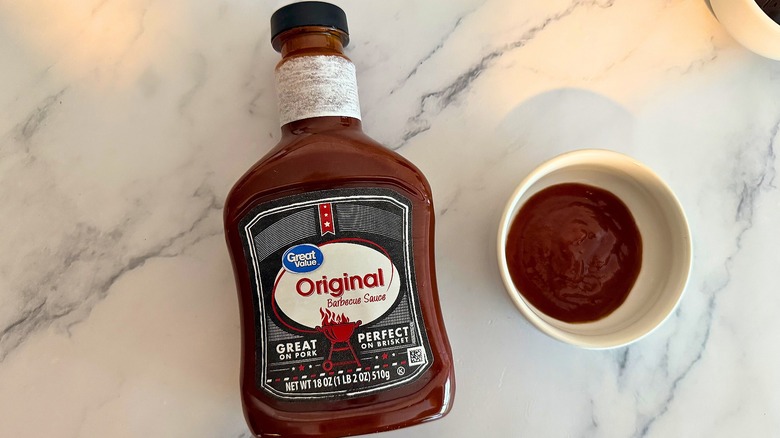 Bottle of Great Value Original BBQ Sauce on table next to small white bowl of sauce