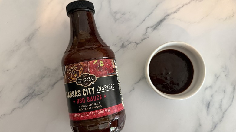 Bottle of Private Selection Kansas City BBQ Sauce on table next to small white bowl of sauce