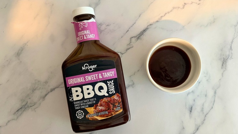 Bottle of Kroger Original Sweet & Tangy BBQ Sauce on table next to small white bowl of sauce