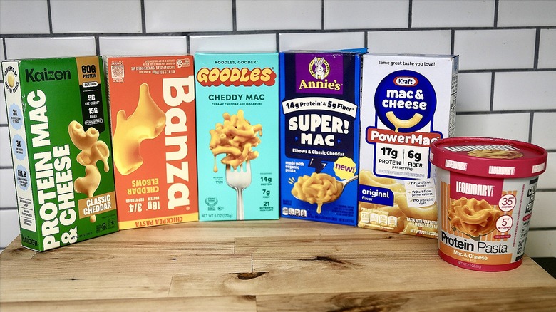 six boxes of protein mac and cheese lined on a counter with a white tile backsplash
