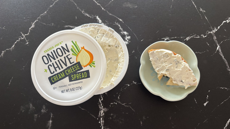 Trader Joe's onion and chive cream cheese container next to bagel piece on plate
