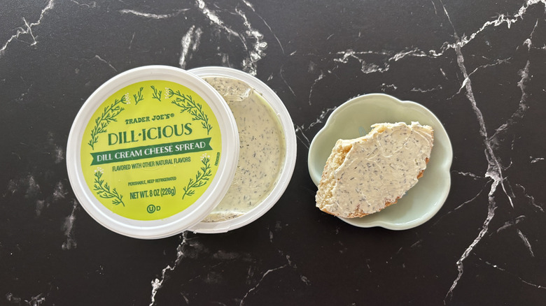 Trader Joe's dill cream cheese container next to bagel piece on plate