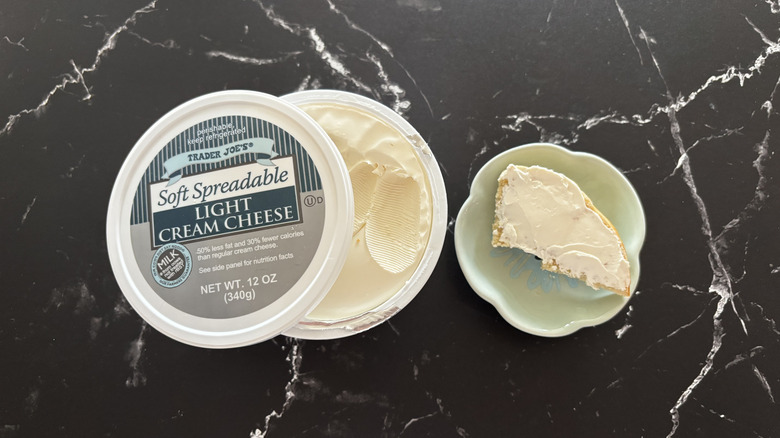Trader Joe's light cream cheese container next to bagel piece on plate