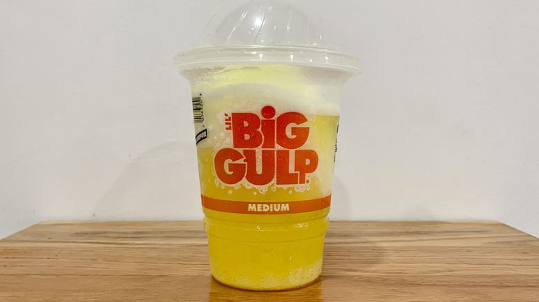 Tropical Twist Slurpee in plastic cup on wooden shelf with white background