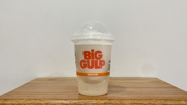 Piña Colada Slurpee in plastic cup on wooden shelf with white background