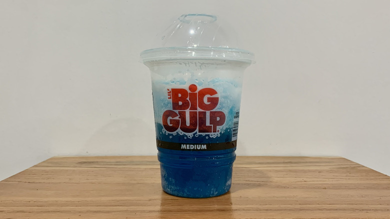Blue Raspberry Slurpee in plastic cup on wooden shelf with white background