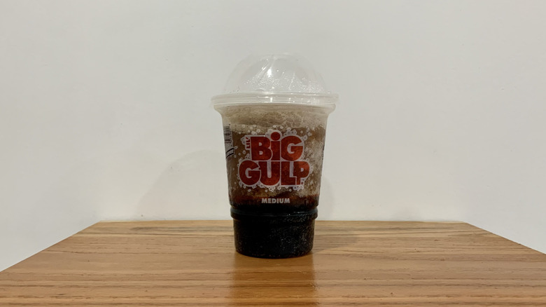 Coca Cola Slurpee in plastic cup on wooden shelf with white background