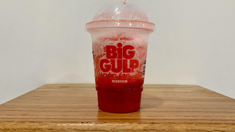 Cherry Slurpee in plastic cup on wooden shelf with white background