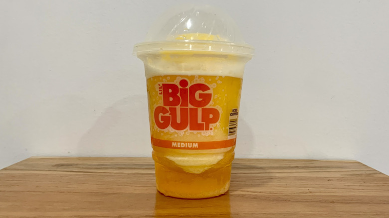 Blood Orange Slurpee in plastic cup on wooden shelf with white background